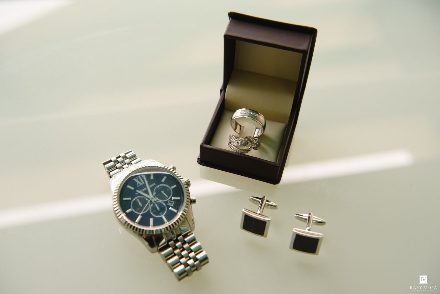 Silver chronograph watch with blue dial beside a jewelry box and square cufflinks on a white surface.