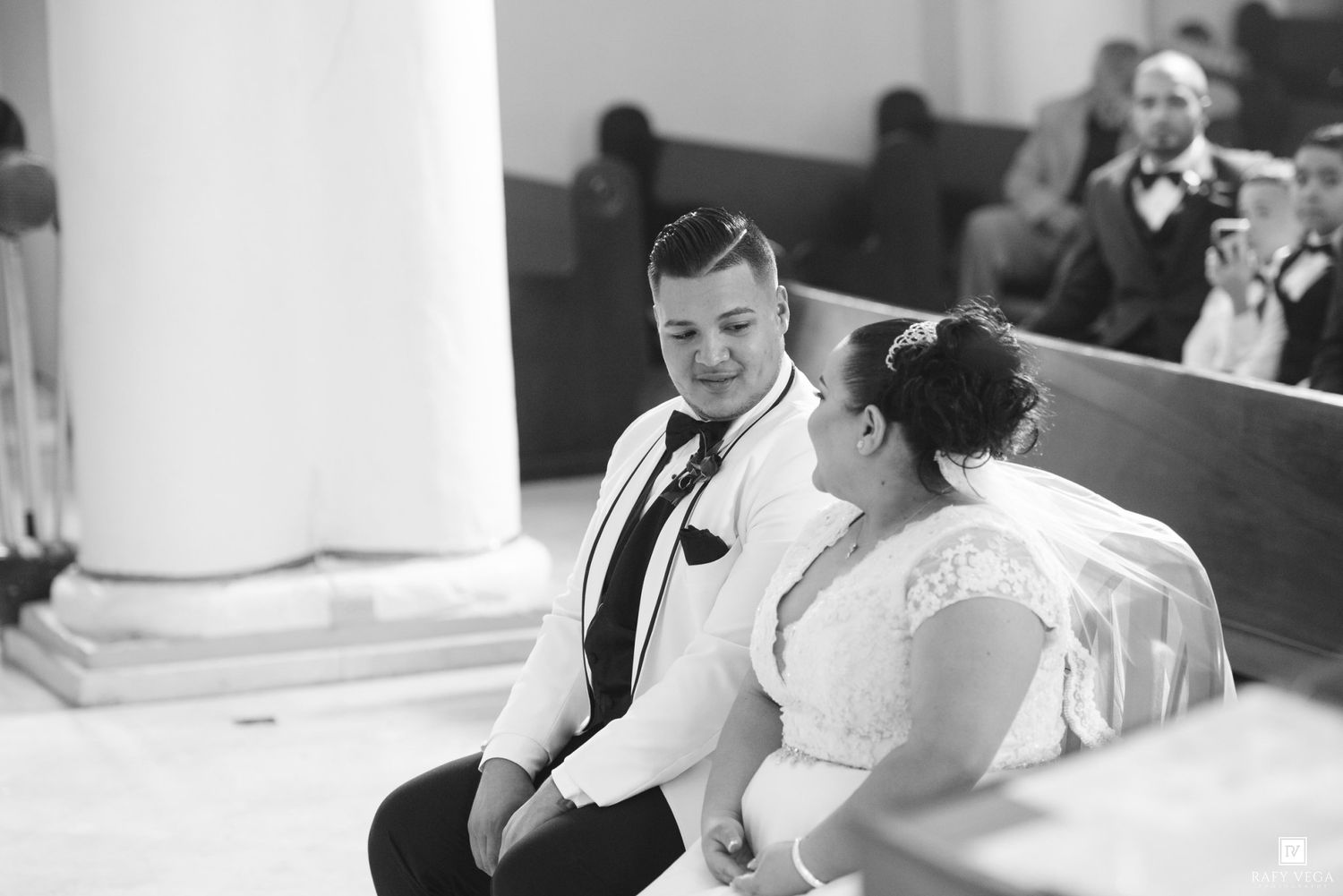 Bride and groom share an intimate moment seated together in a church pew during their wedding ceremony.