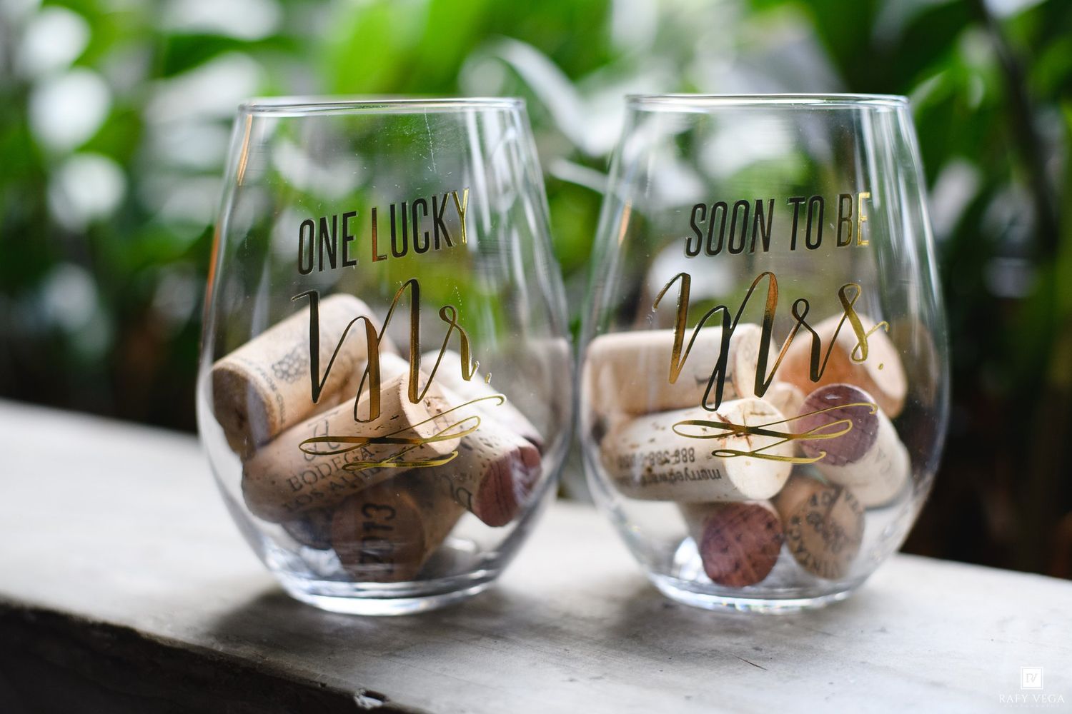 Two stemless wine glasses reading One Lucky Mr and Soon to Be Mrs filled with corks for an engagement celebration.