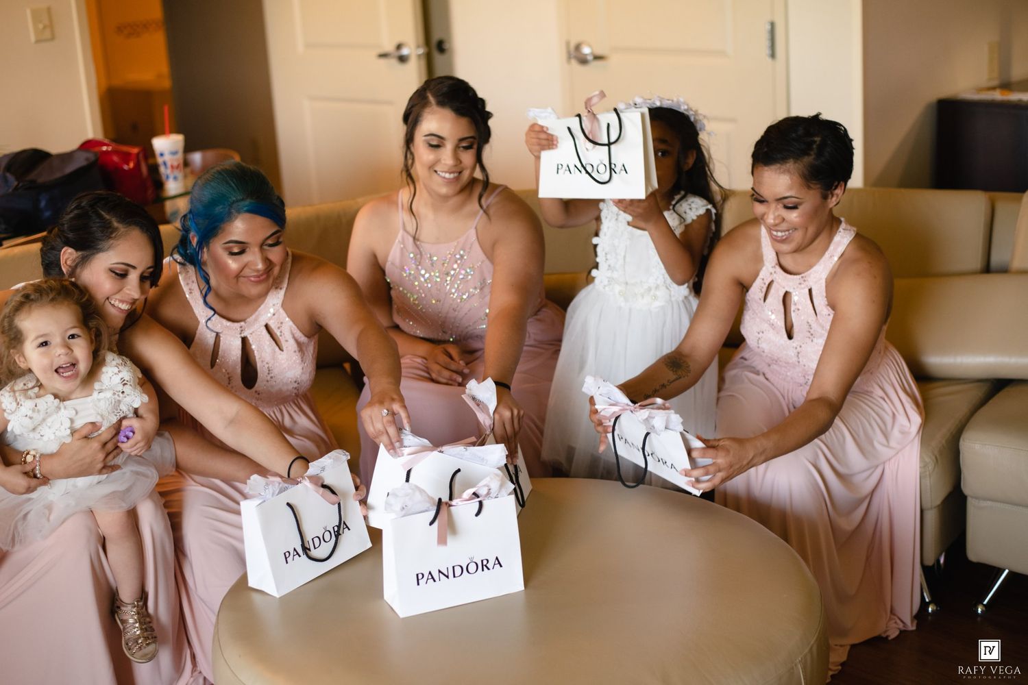 Bridesmaids in blush pink dresses opening Pandora gift bags together before a wedding ceremony.