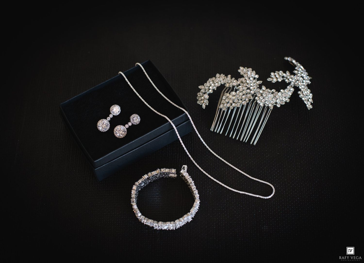 Elegant bridal jewelry set featuring crystal earrings, bracelet, hair comb, and delicate necklace on dark velvet background.