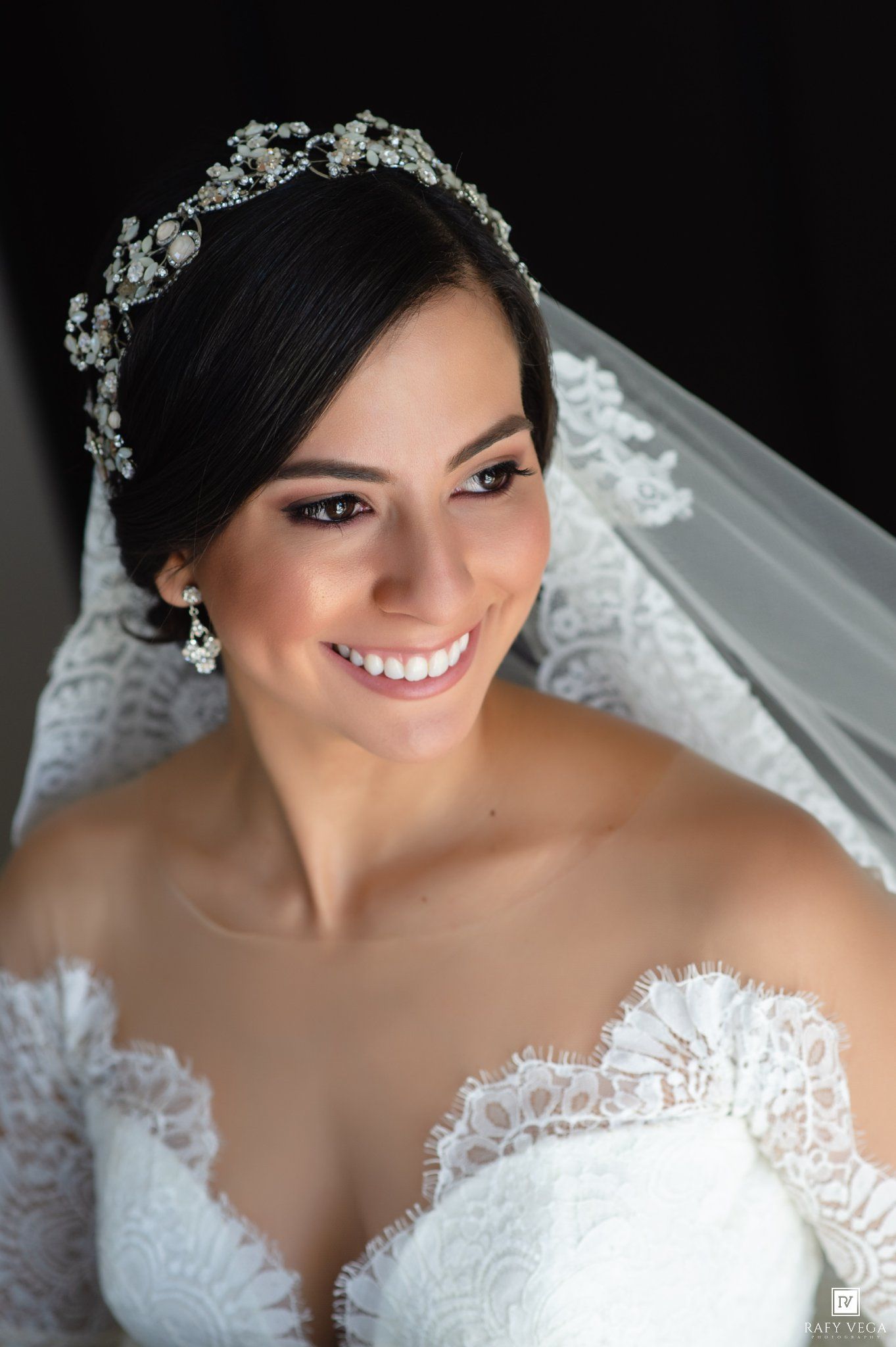 Smiling bride wearing a crystal tiara, veil, and lace wedding dress poses for a elegant bridal portrait photo.