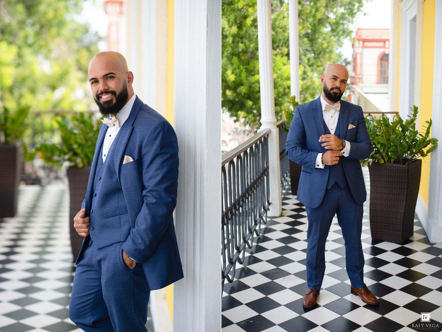 Bald man with beard in navy blue suit posing on checkered floor balcony with white columns.