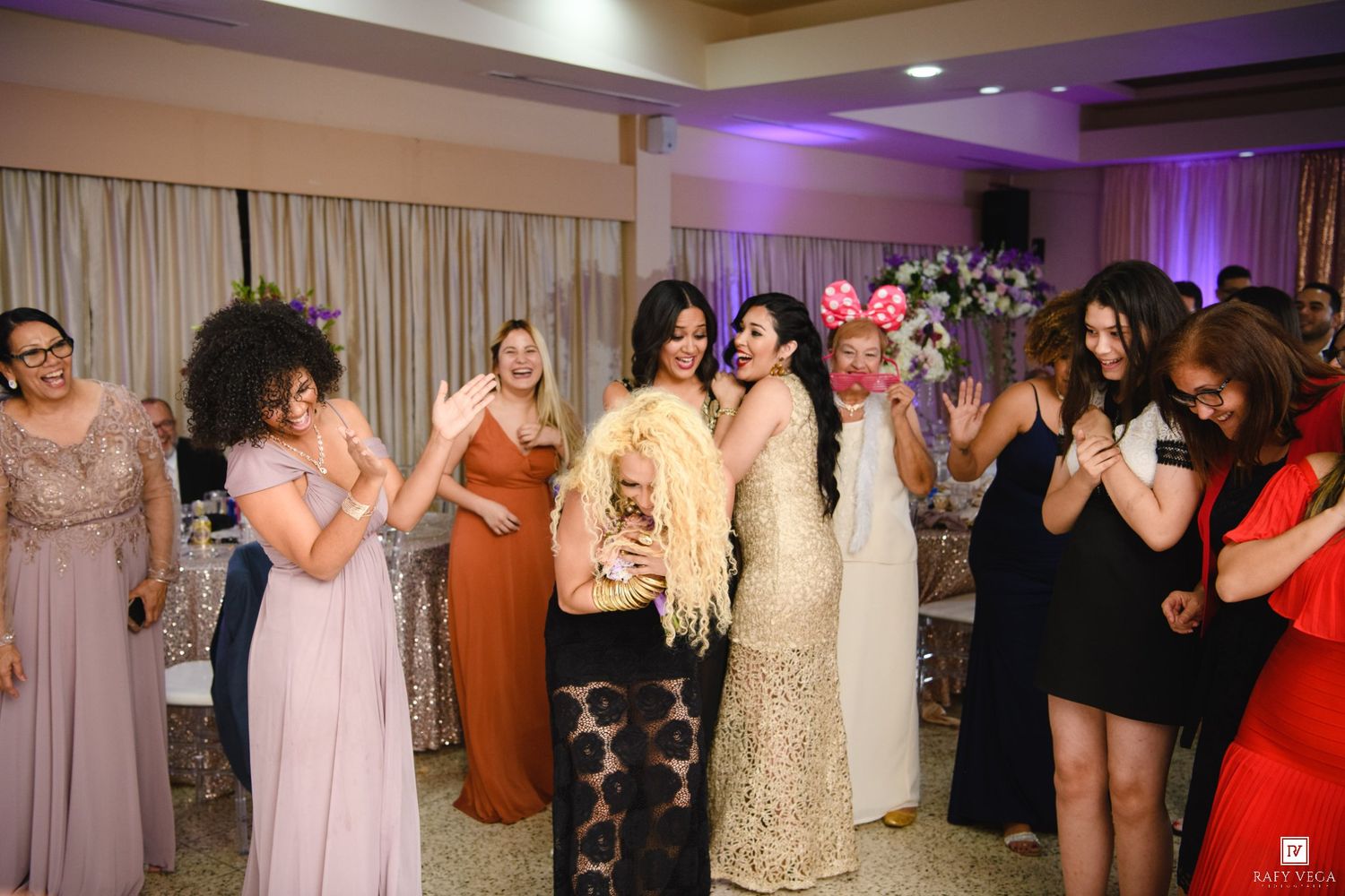 Women in elegant dresses celebrating at a wedding reception, laughing and dancing together in a decorated banquet hall.