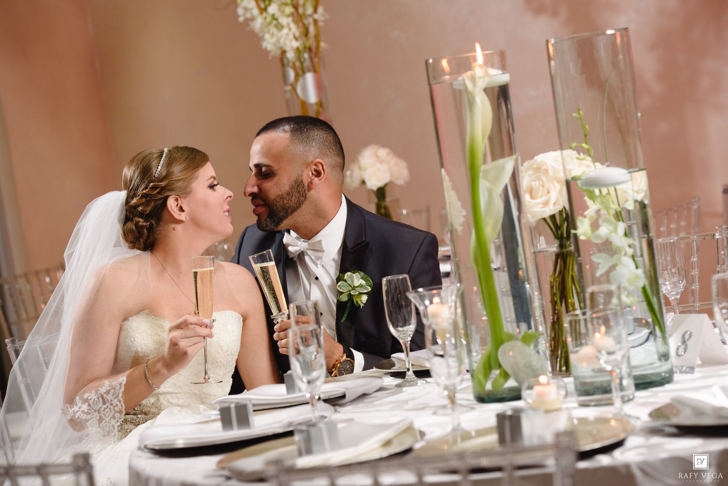 Bride and groom share a romantic moment at elegantly decorated reception dinner table.