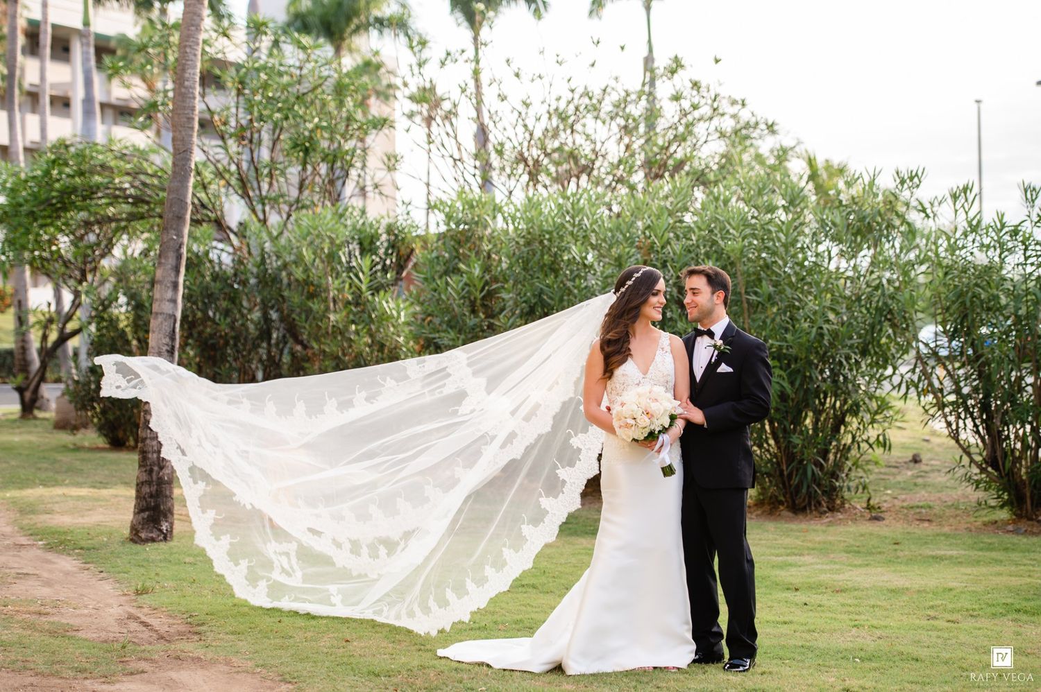 Bride and groom share a romantic moment outdoors as her cathedral lace veil billows in the breeze.