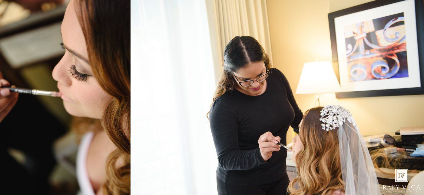 Bride getting makeup applied while stylist adjusts floral hair accessory on veil during wedding preparation.