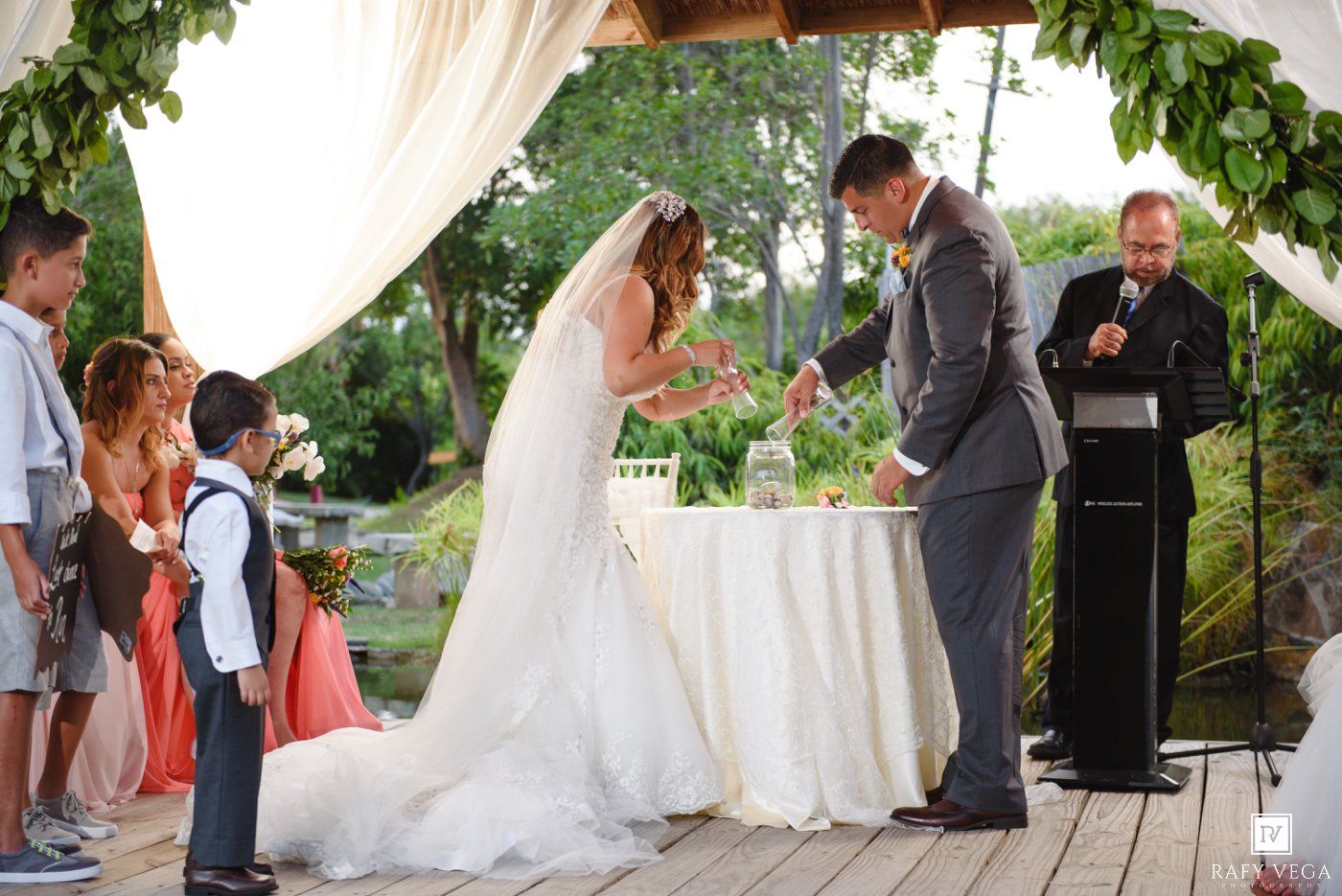 Bride and groom exchange rings during an elegant outdoor wedding ceremony with officiant.