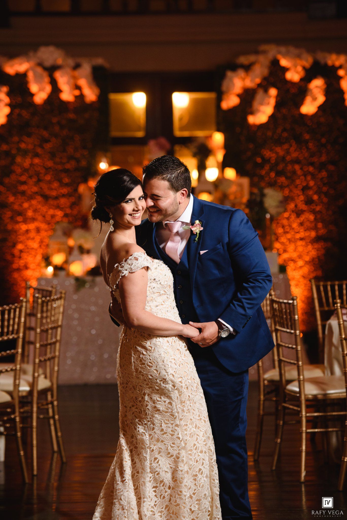 Bride and groom share a romantic dance at elegant wedding reception with warm floral backdrop and golden candlelight.