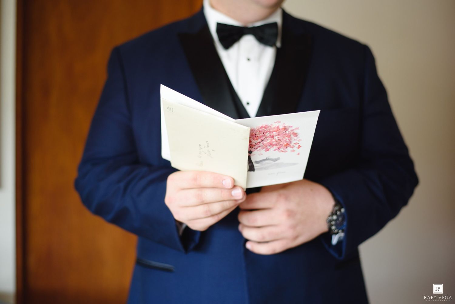 Groom in navy tuxedo reading a wedding card before the ceremony.