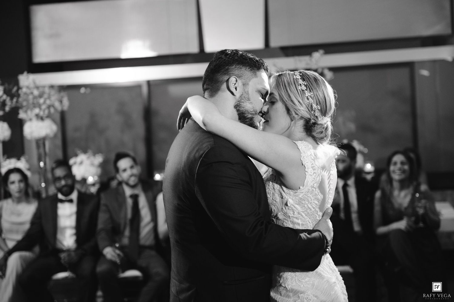 A bride and groom share their first kiss at a wedding ceremony while guests watch in the background.