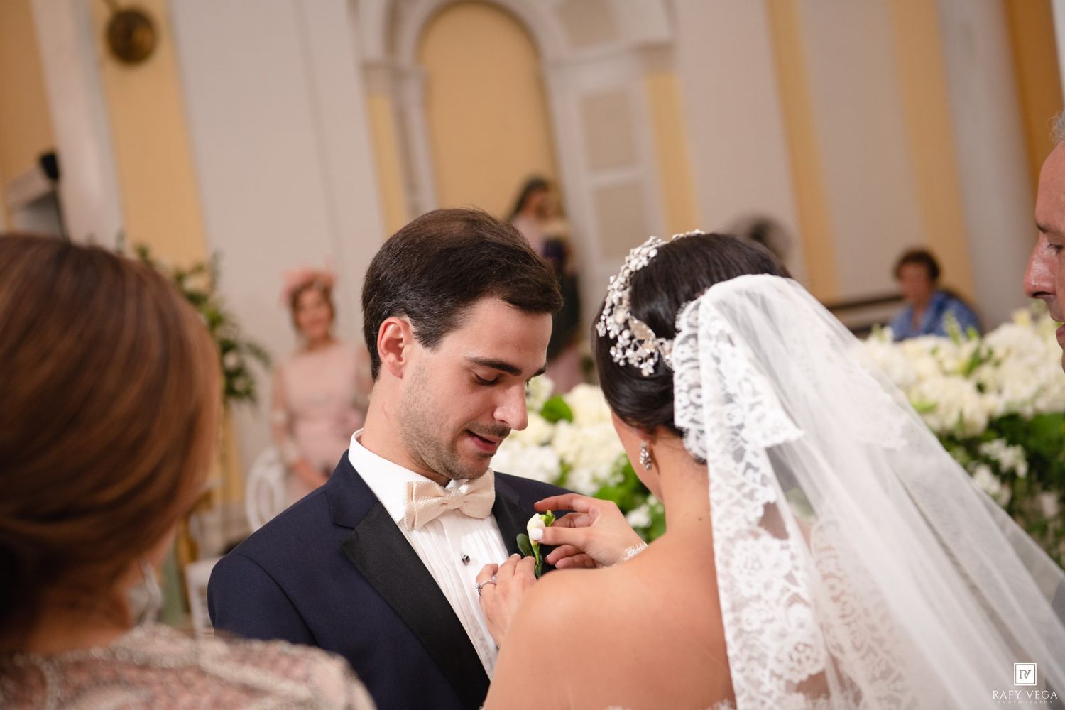 Groom smiling as bride pins boutonniere during elegant church wedding ceremony.