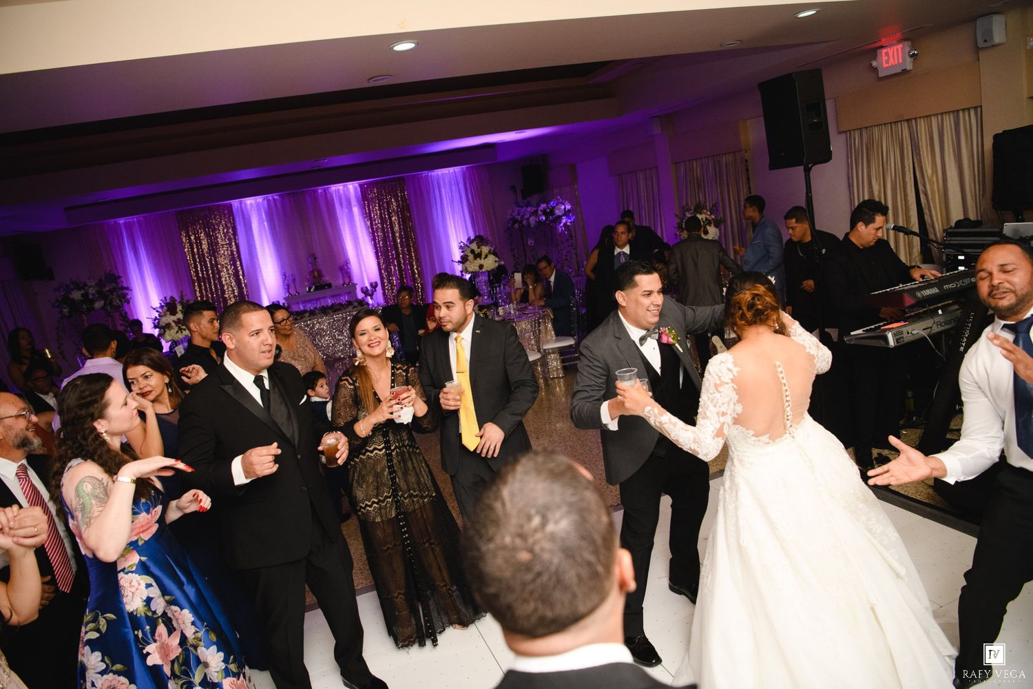 Guests and wedding party dance together at a lively evening wedding reception celebration.