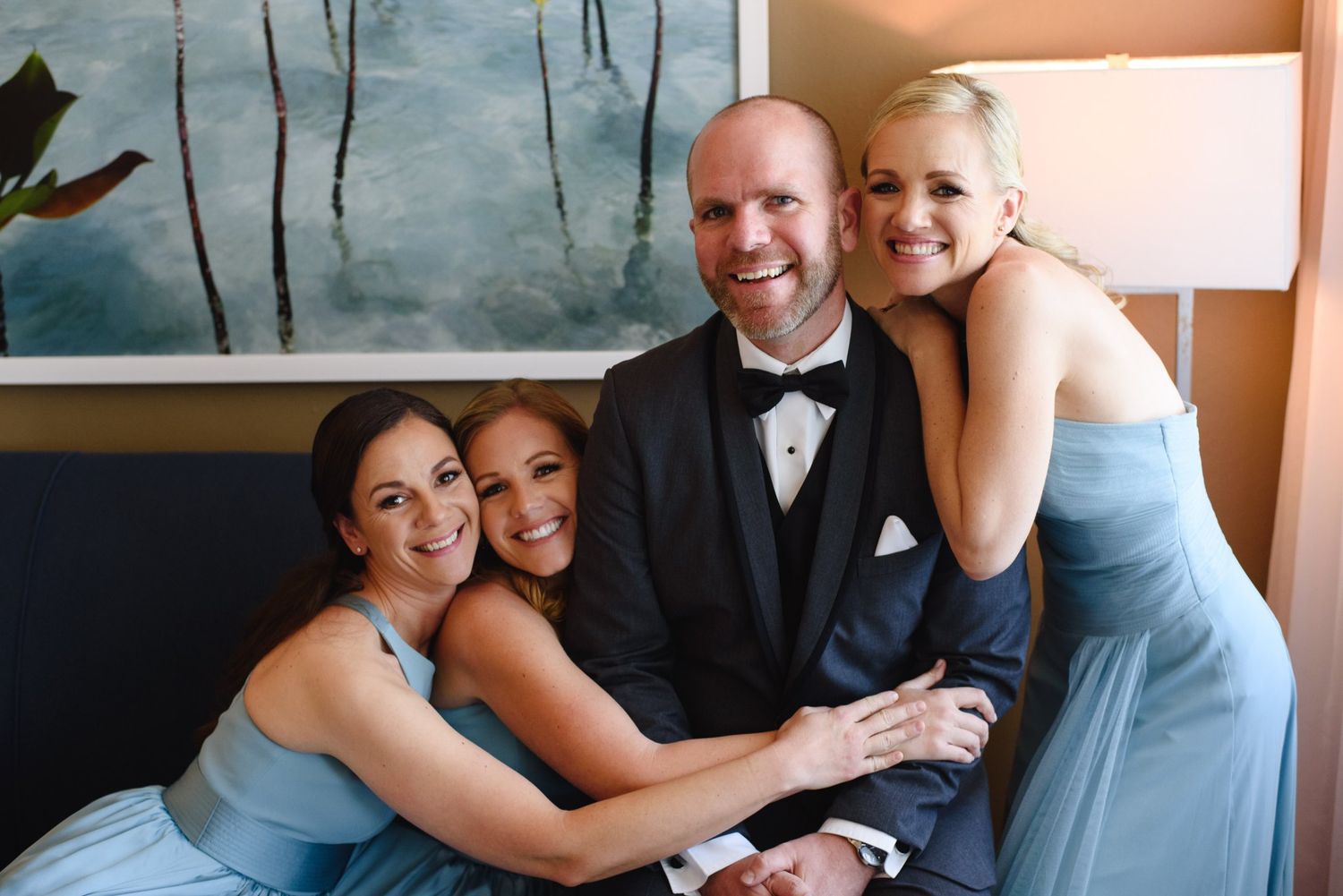 A smiling man in a tuxedo poses with three bridesmaids in light blue gowns at a wedding celebration.