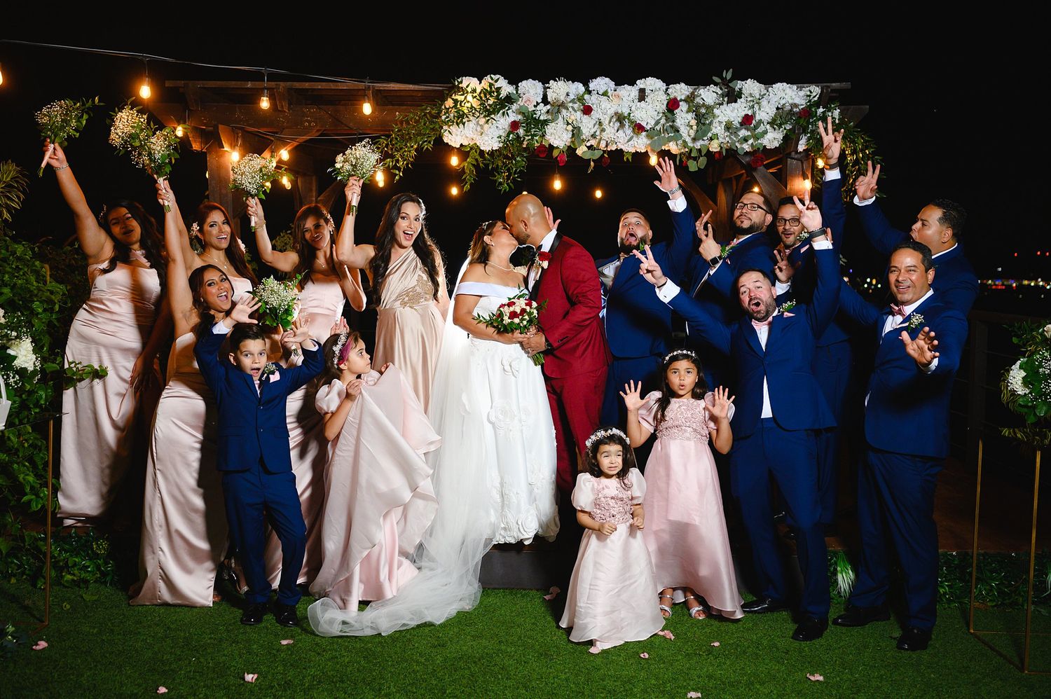 Joyful wedding party celebrating outdoors with bridesmaids in blush, groomsmen in navy suits.
