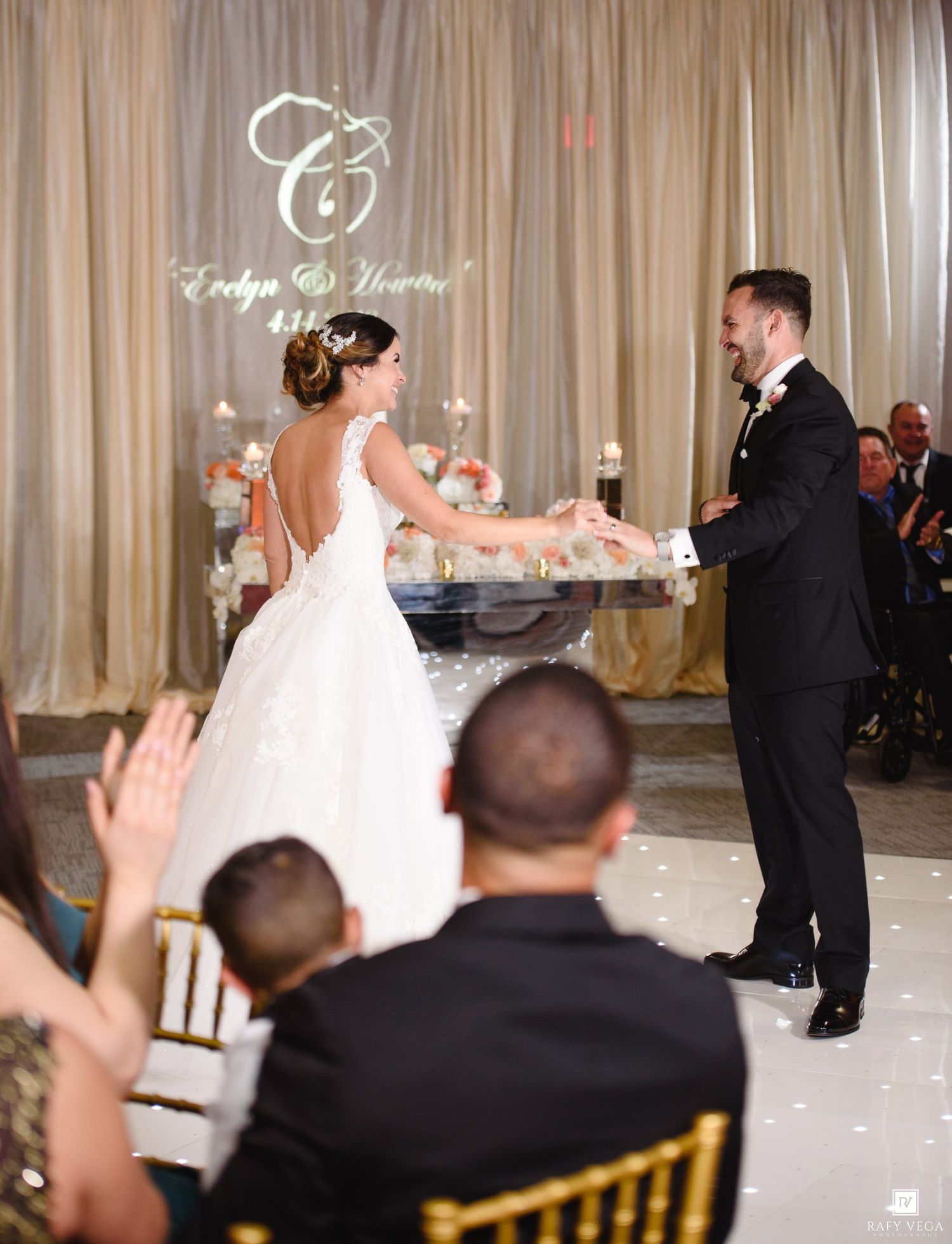 Bride and groom share their first dance at elegant wedding reception with monogram backdrop.