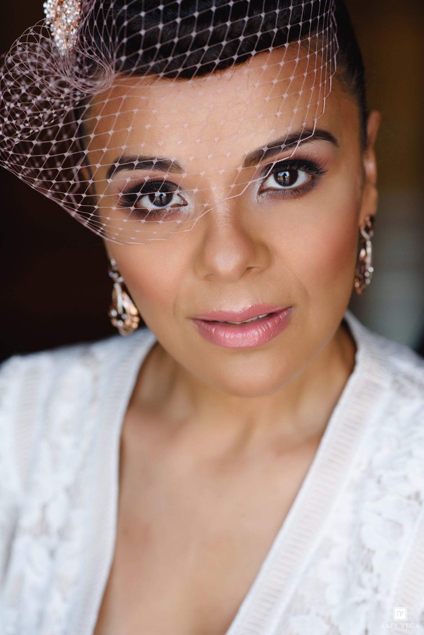Close-up portrait of a bride wearing a birdcage veil, elegant earrings, and natural glam makeup.