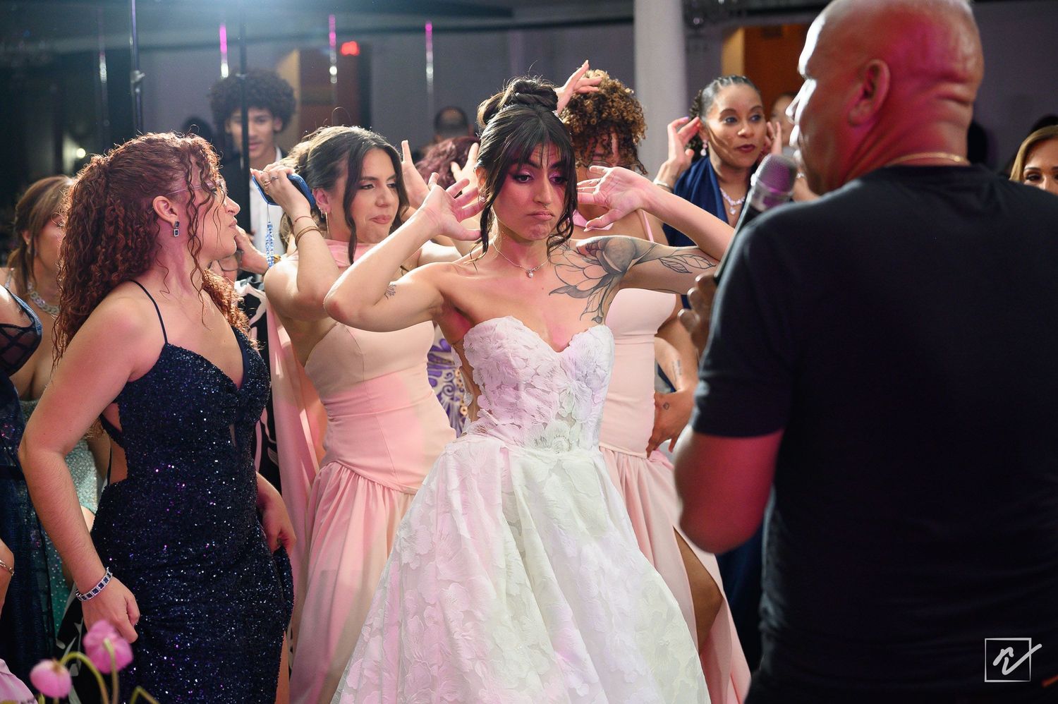 Bride in a white strapless ball gown dances joyfully at her wedding reception surrounded by bridesmaids in pink and black dresses.