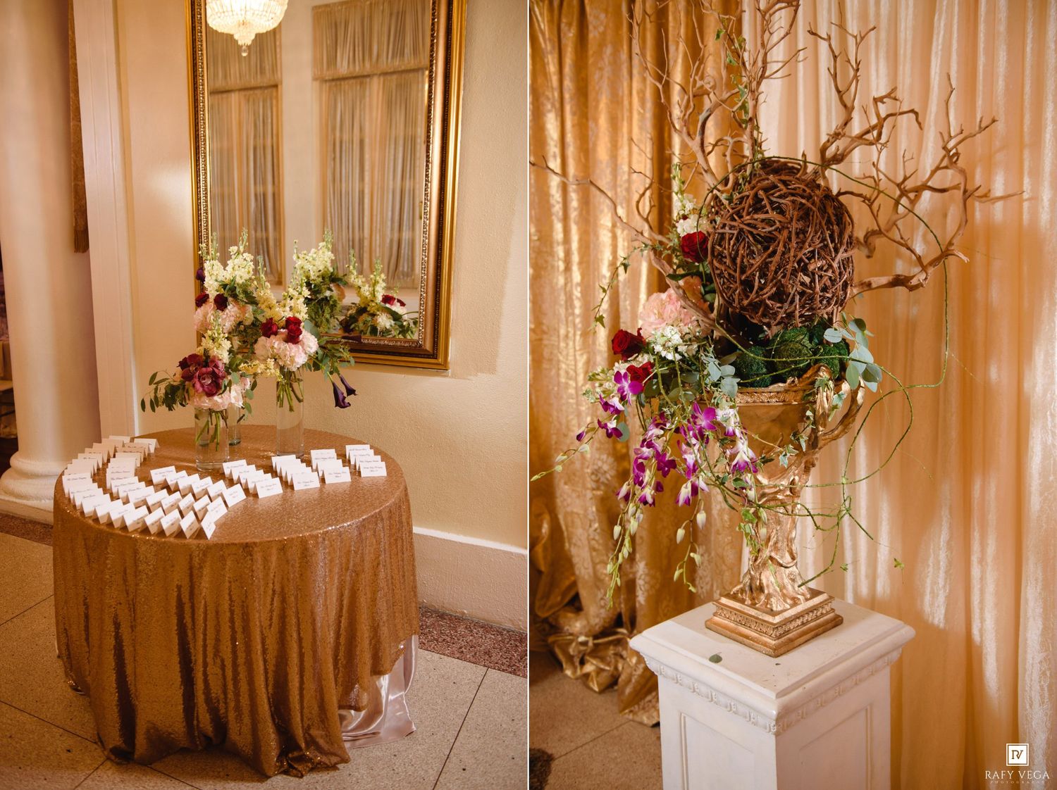 Elegant wedding reception escort card table with gold tablecloth and floral centerpiece beside ornate urn with branches.