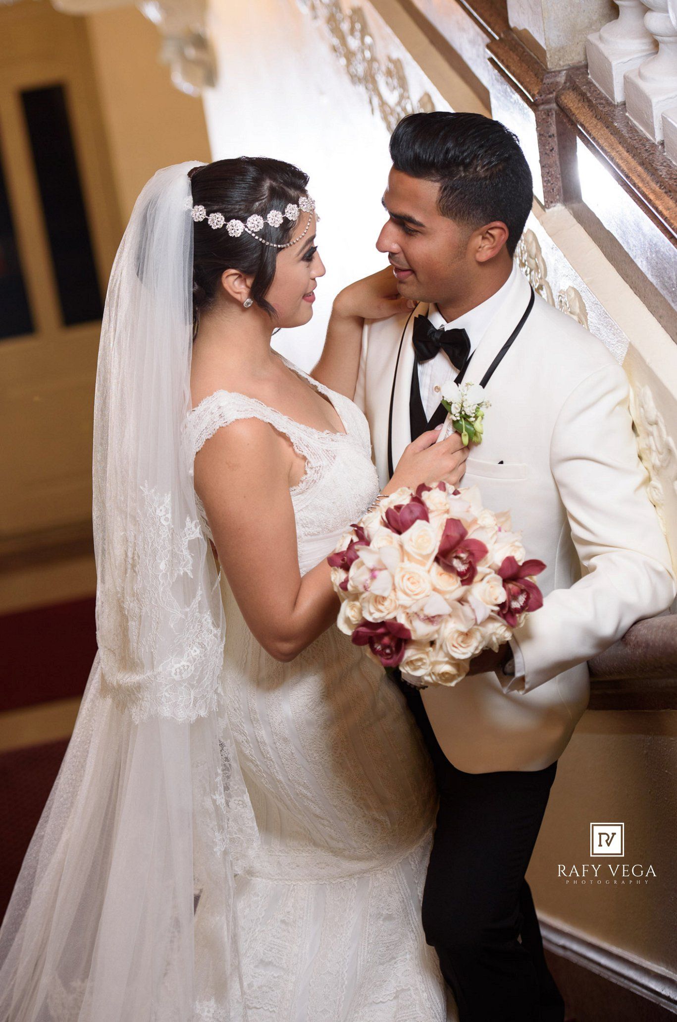 Bride and groom in elegant wedding attire share a romantic moment on a staircase, bride holding a bouquet.