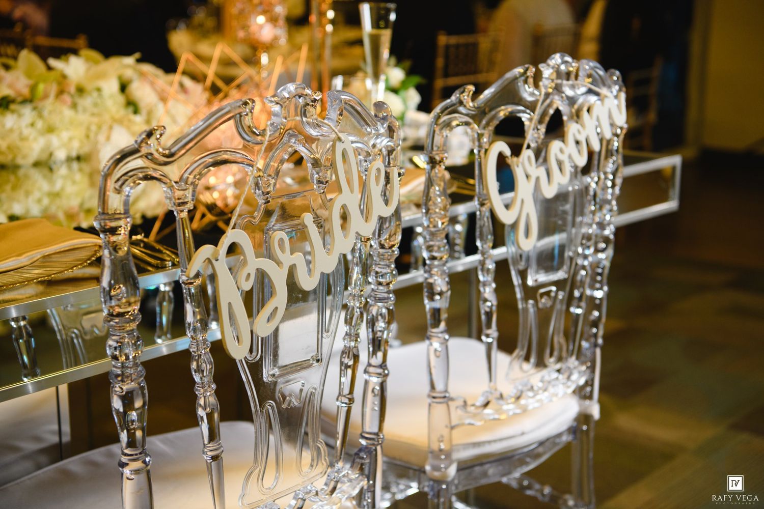 Elegant acrylic bride and groom chairs with cursive name signs at a luxury wedding reception.