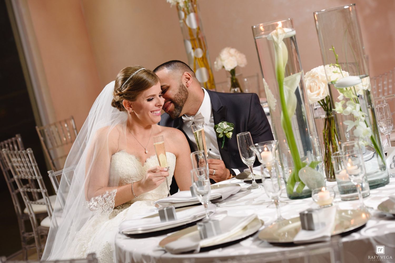 Bride and groom share a romantic moment at their elegant wedding reception table adorned with floral centerpieces.