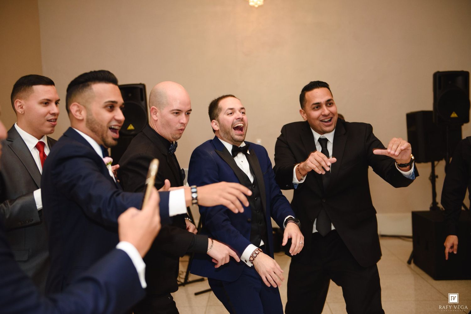 Groom and groomsmen laughing and celebrating together in suits at a wedding reception.