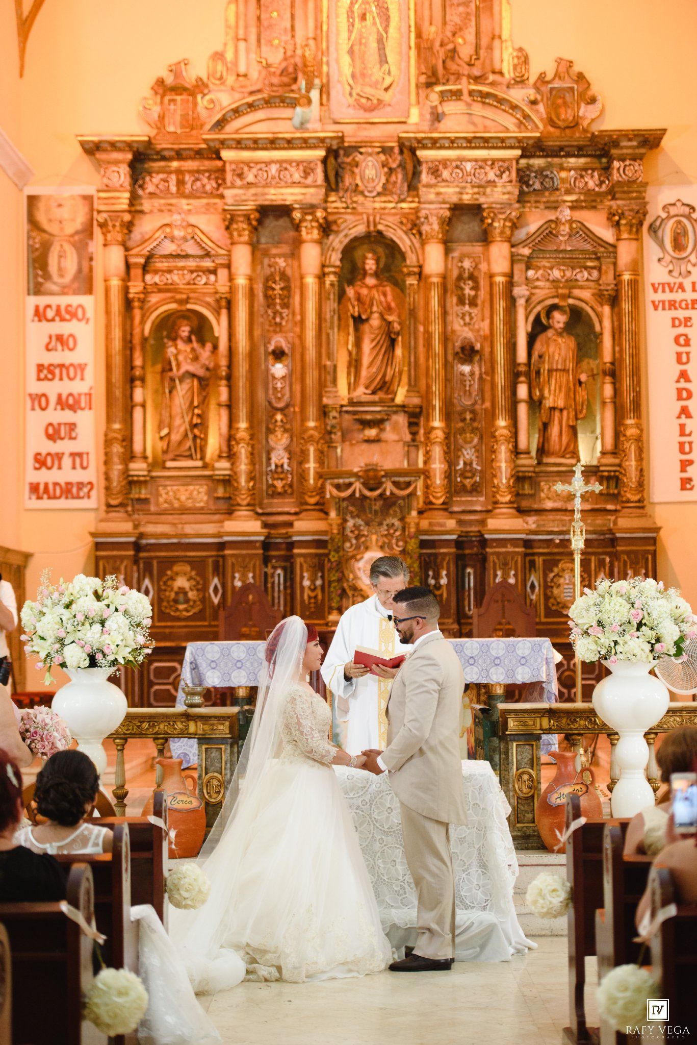 Bride and groom exchange vows at ornate golden altar in a Catholic church wedding ceremony.