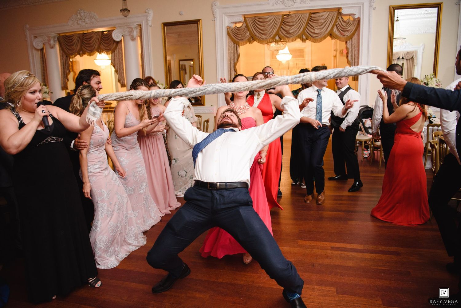 Wedding guests doing the limbo dance at a lively reception in an elegant ballroom venue.