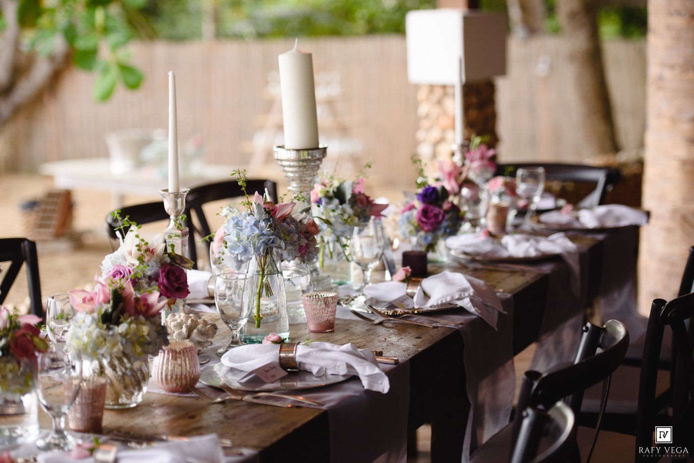 Elegant outdoor wedding reception table set with floral centerpieces, candles, and fine dinnerware.