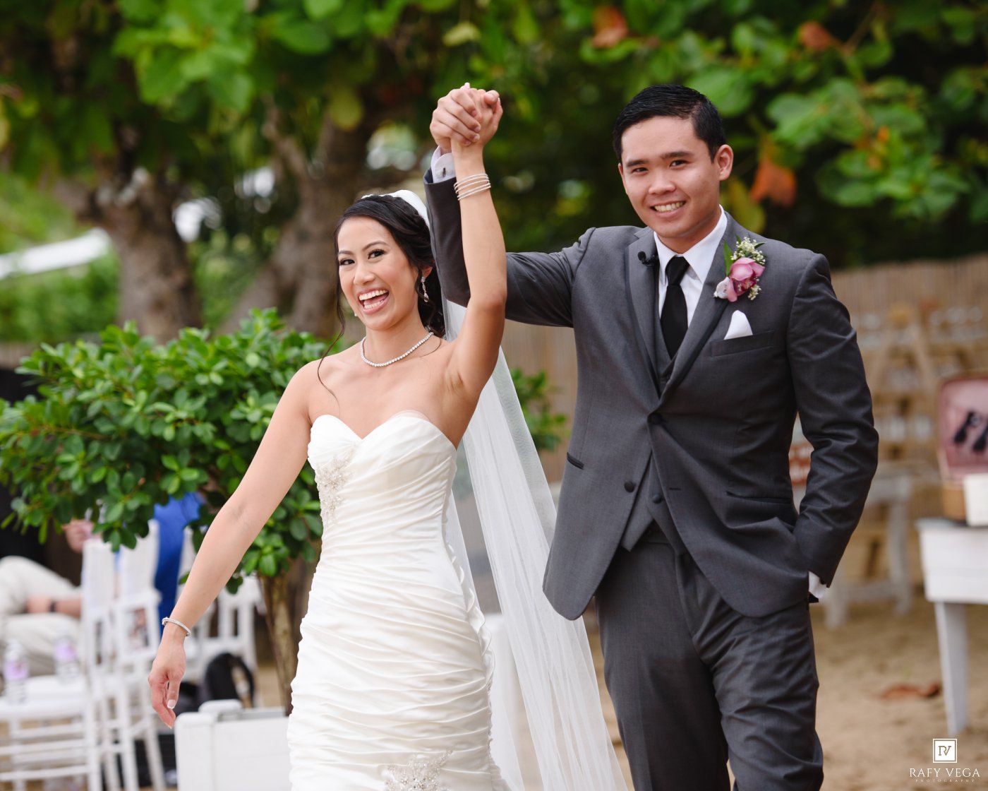 Newlywed couple walks triumphantly hand-in-hand after their outdoor beach wedding ceremony.