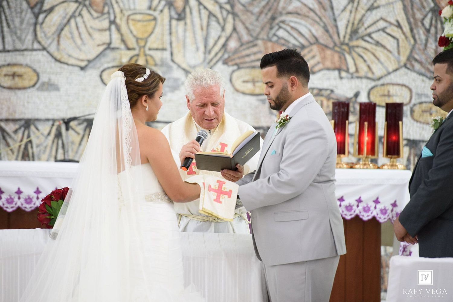 Bride and groom exchanging vows with officiant at a Catholic church wedding ceremony altar.