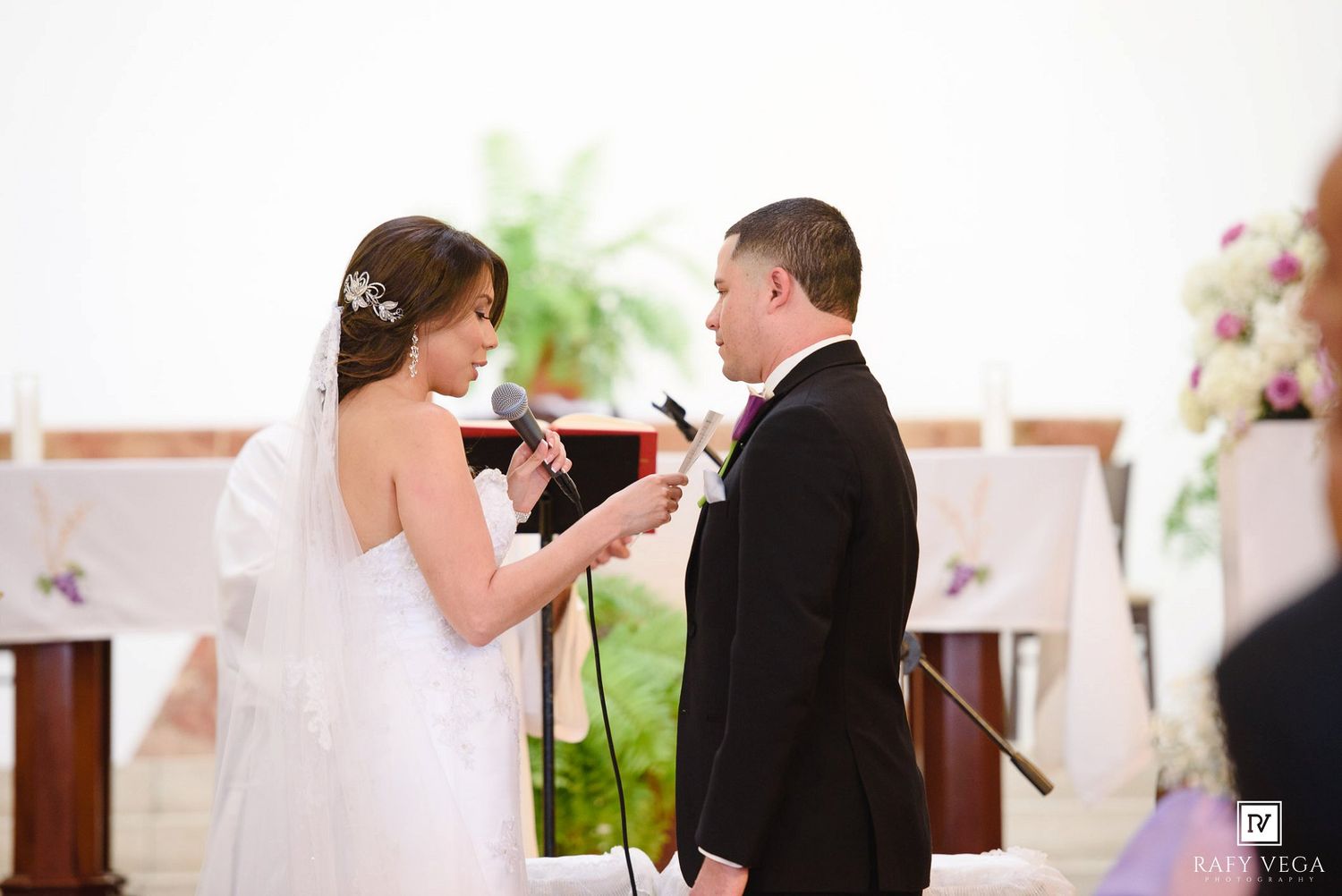 Bride and groom exchanging vows at wedding ceremony altar with microphones and floral decorations.