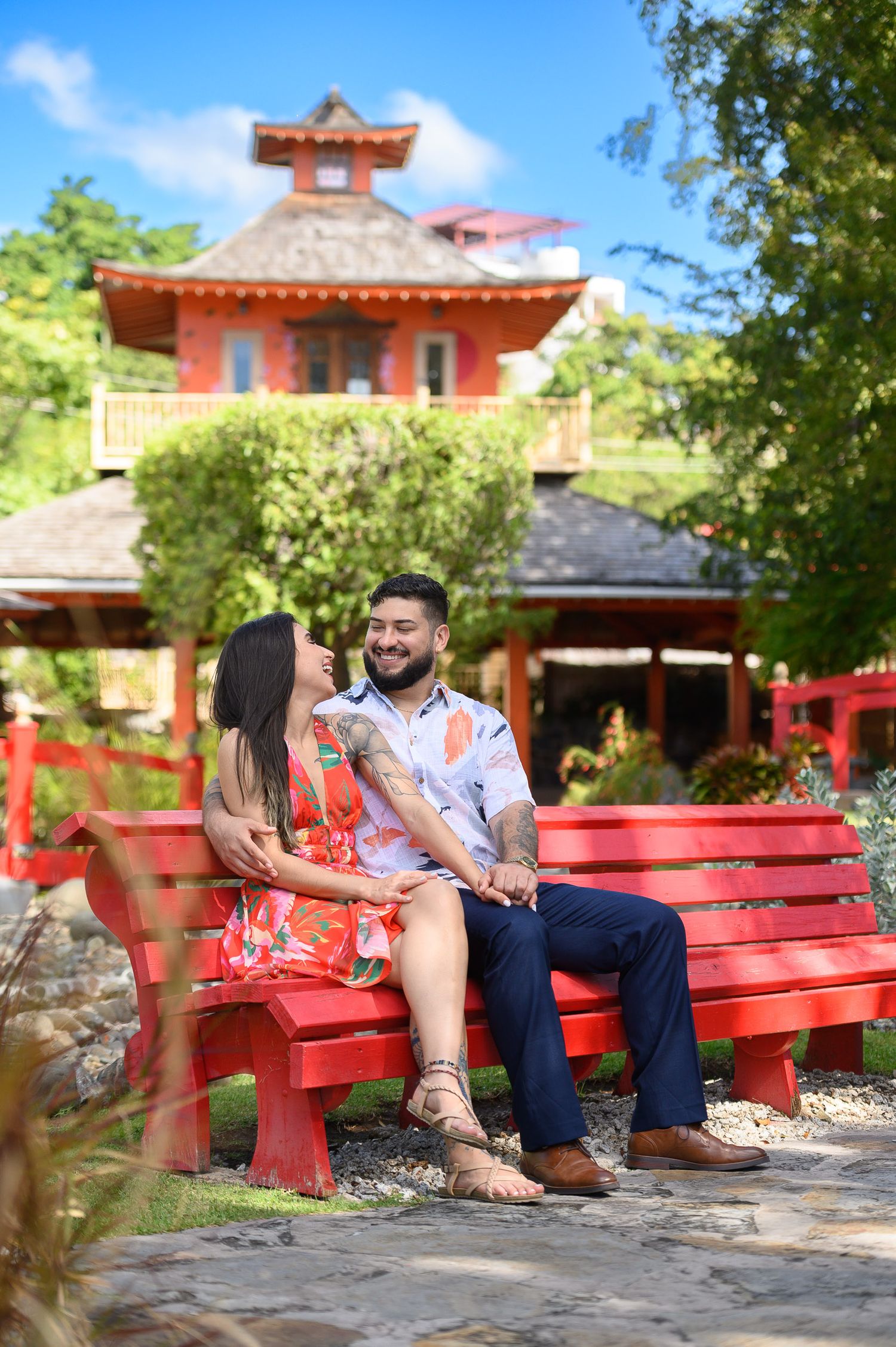 Couple sitting together on a red bench in a lush Japanese garden with a pagoda behind them.