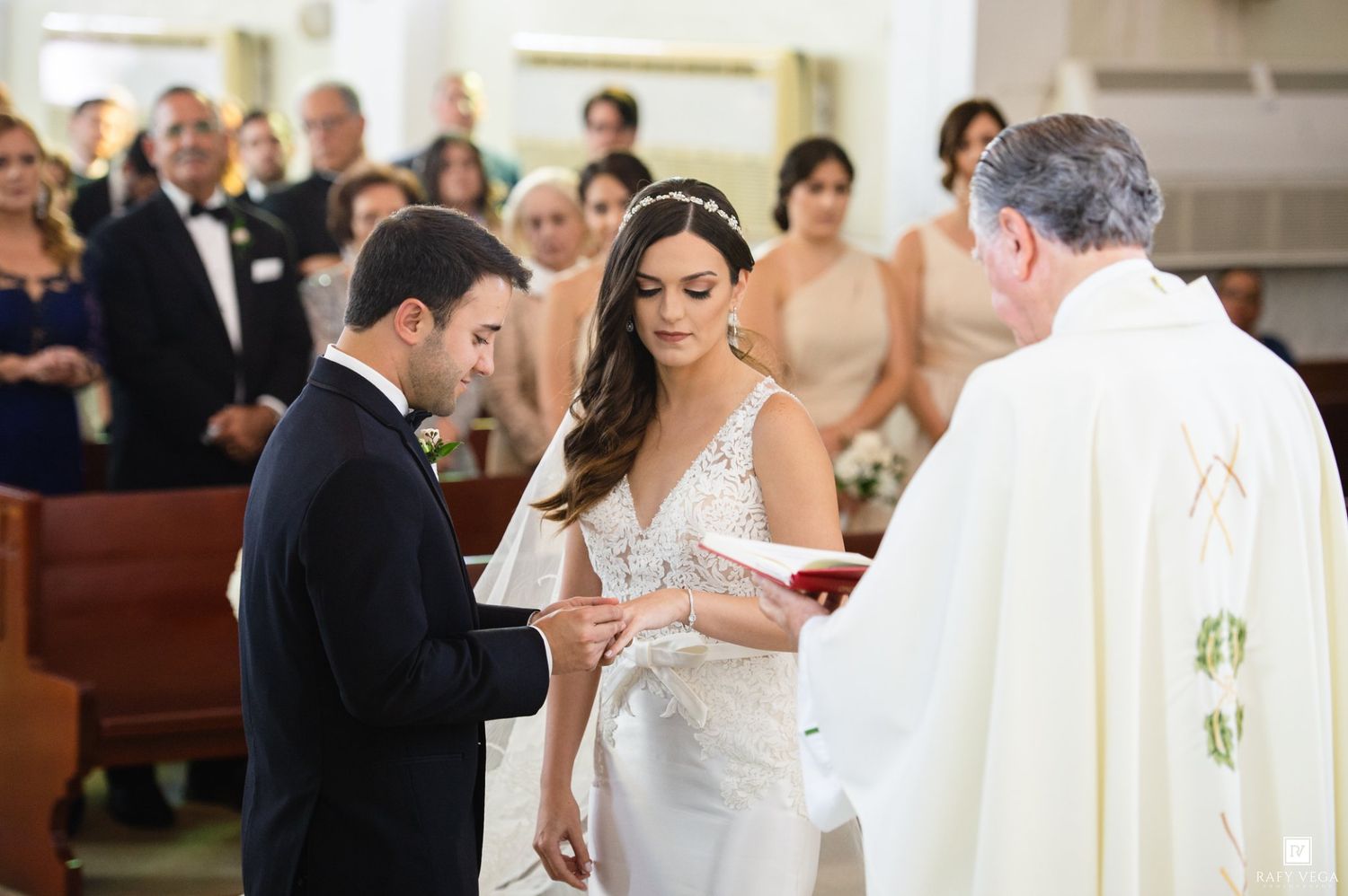 Bride and groom exchanging rings during a Catholic wedding ceremony at the altar with a priest officiating.