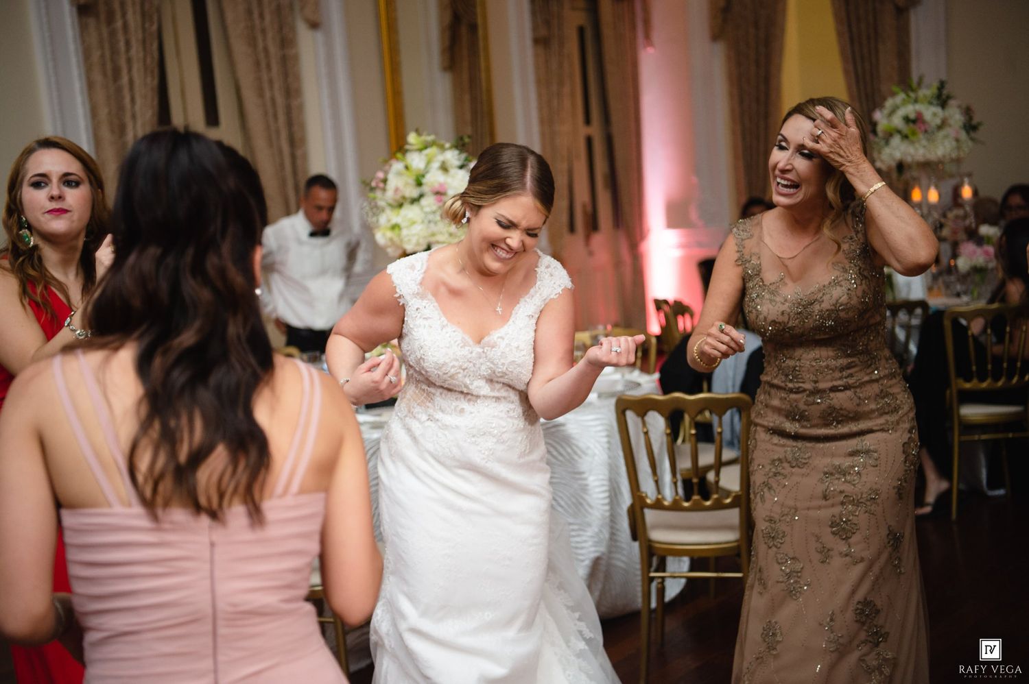 Bride in white gown laughing and dancing with guests at elegant wedding reception.