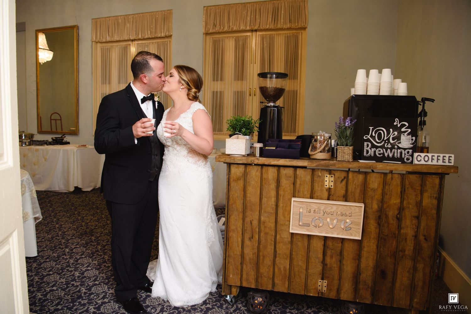 Bride and groom share a tender kiss beside a rustic coffee bar station at their wedding reception.