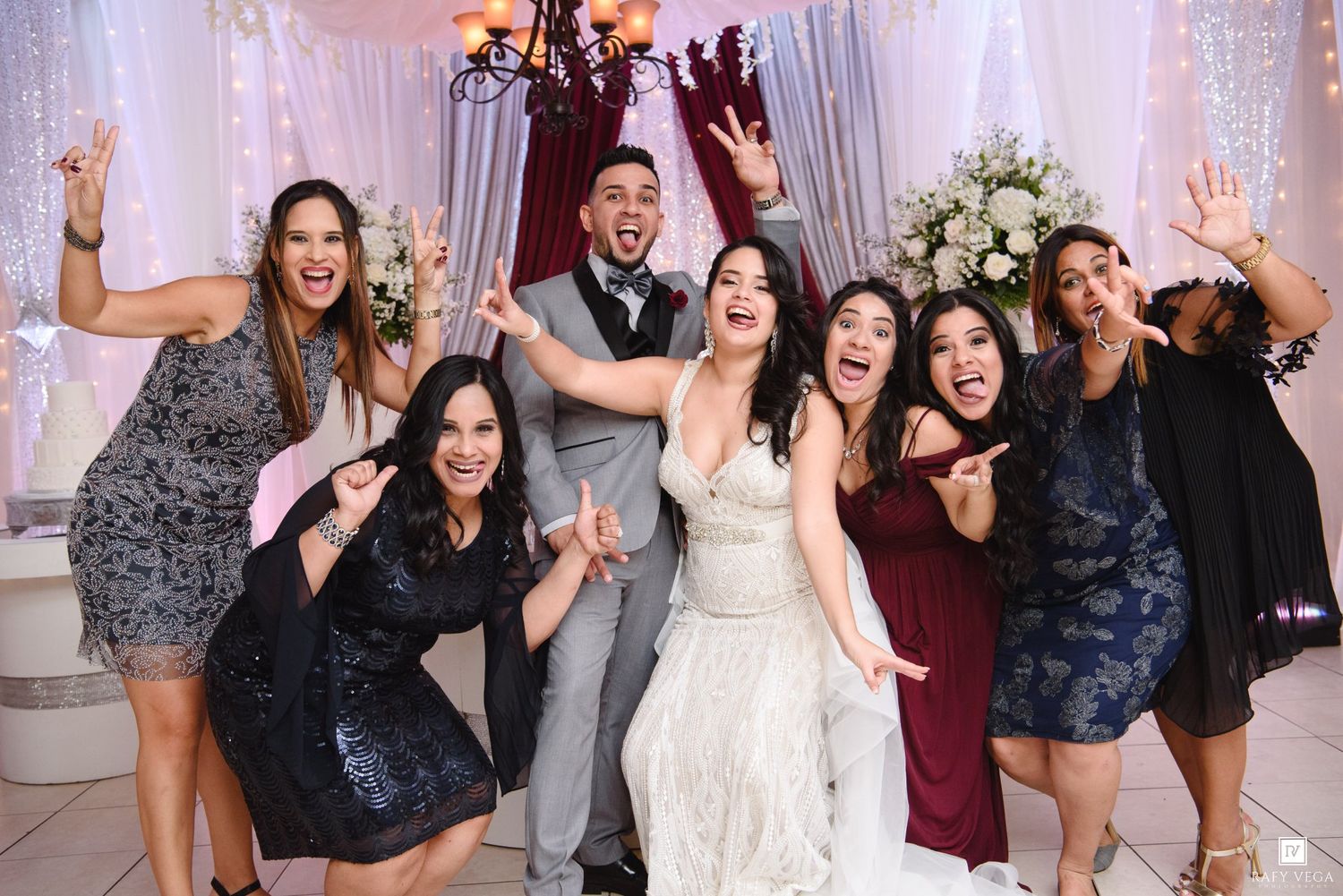 Bride and groom celebrating joyfully with bridesmaids in burgundy dresses at elegant wedding reception.