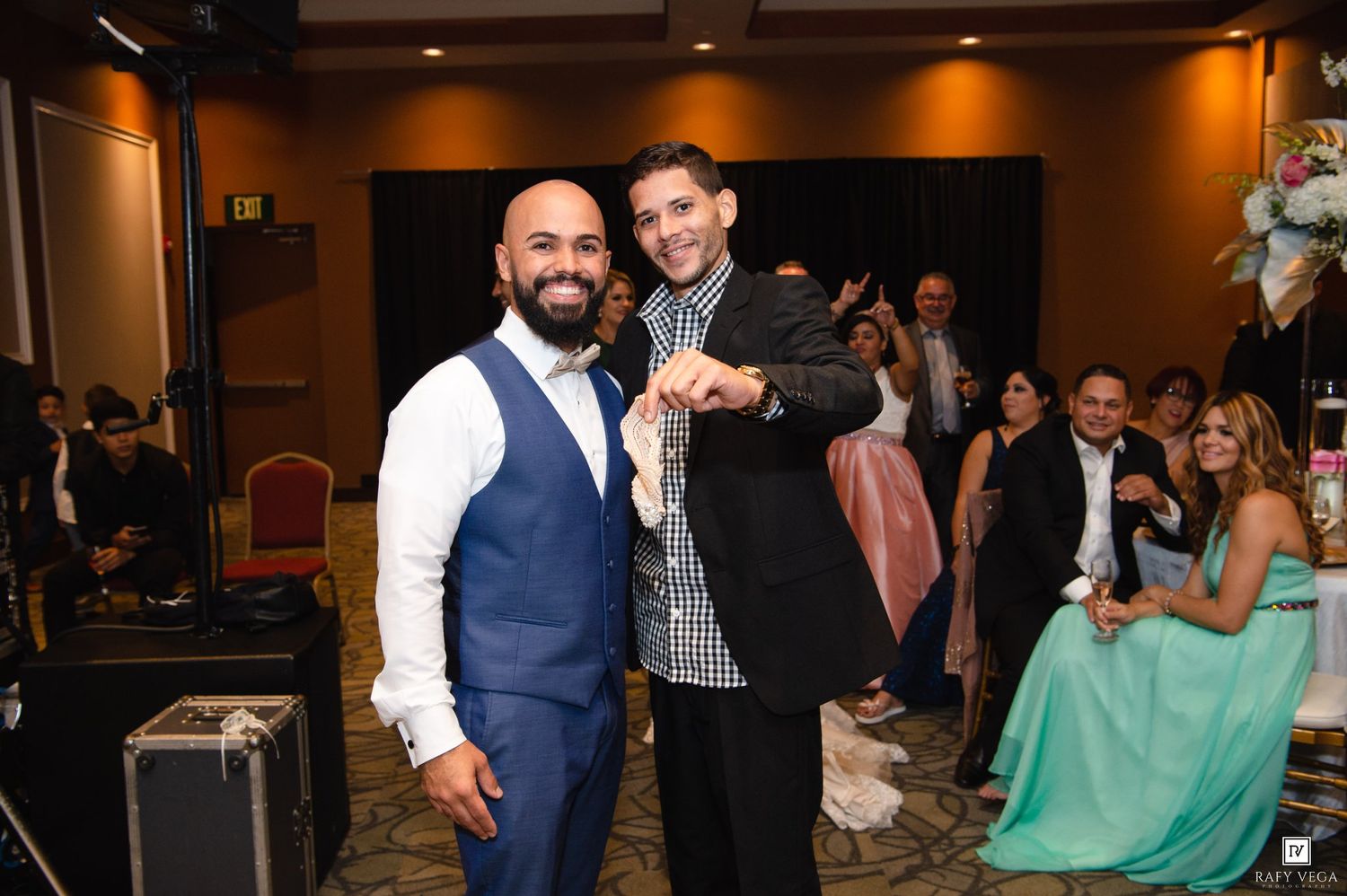 Two men smiling and posing together at a formal event, one in a blue vest and the other in a black blazer.