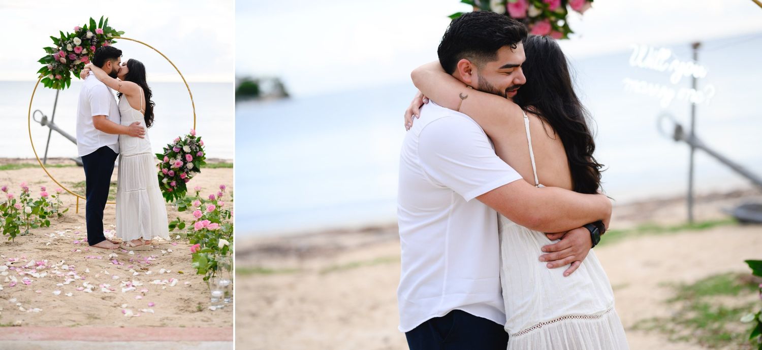 Bride and groom embracing lovingly under a circular floral arch on a sandy beach at their outdoor wedding.