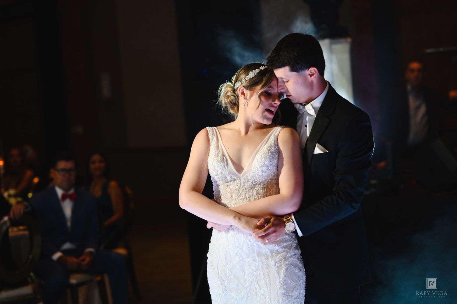 Bride and groom share an intimate first dance at their wedding reception, with guests watching in the background.