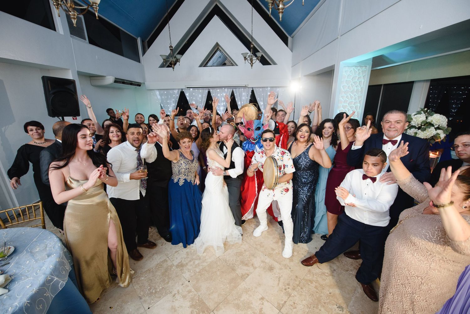 Wedding reception group photo with bride, groom, and guests celebrating joyfully in an elegant decorated venue.