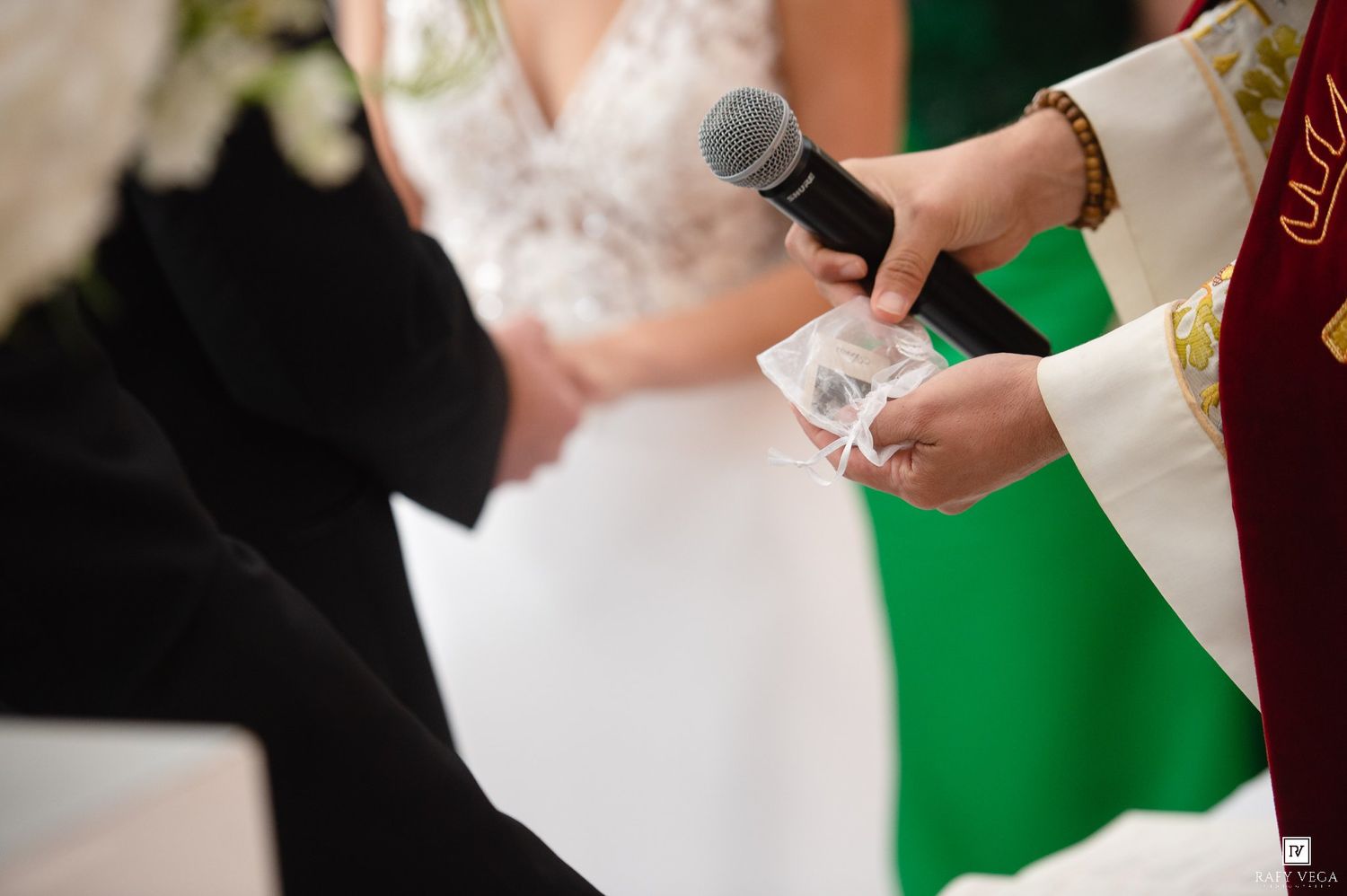Officiant holds wedding rings on a pillow and microphone during a formal wedding ceremony.