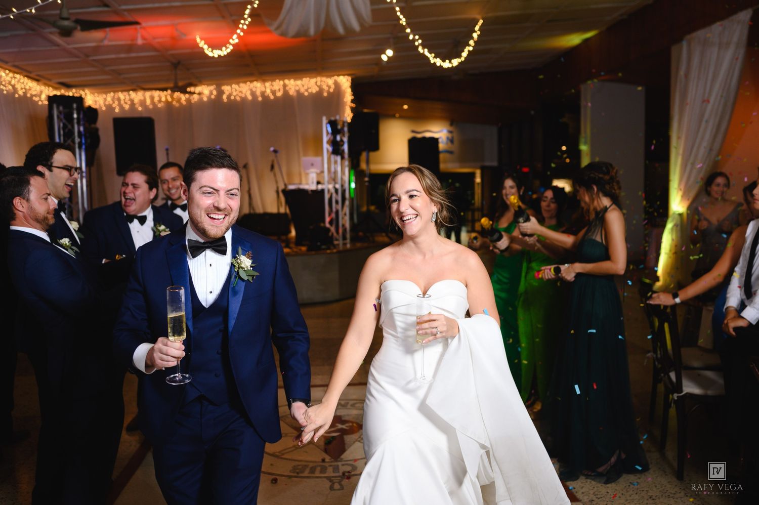 Happy bride and groom holding hands and champagne as they make their grand entrance at their wedding reception.
