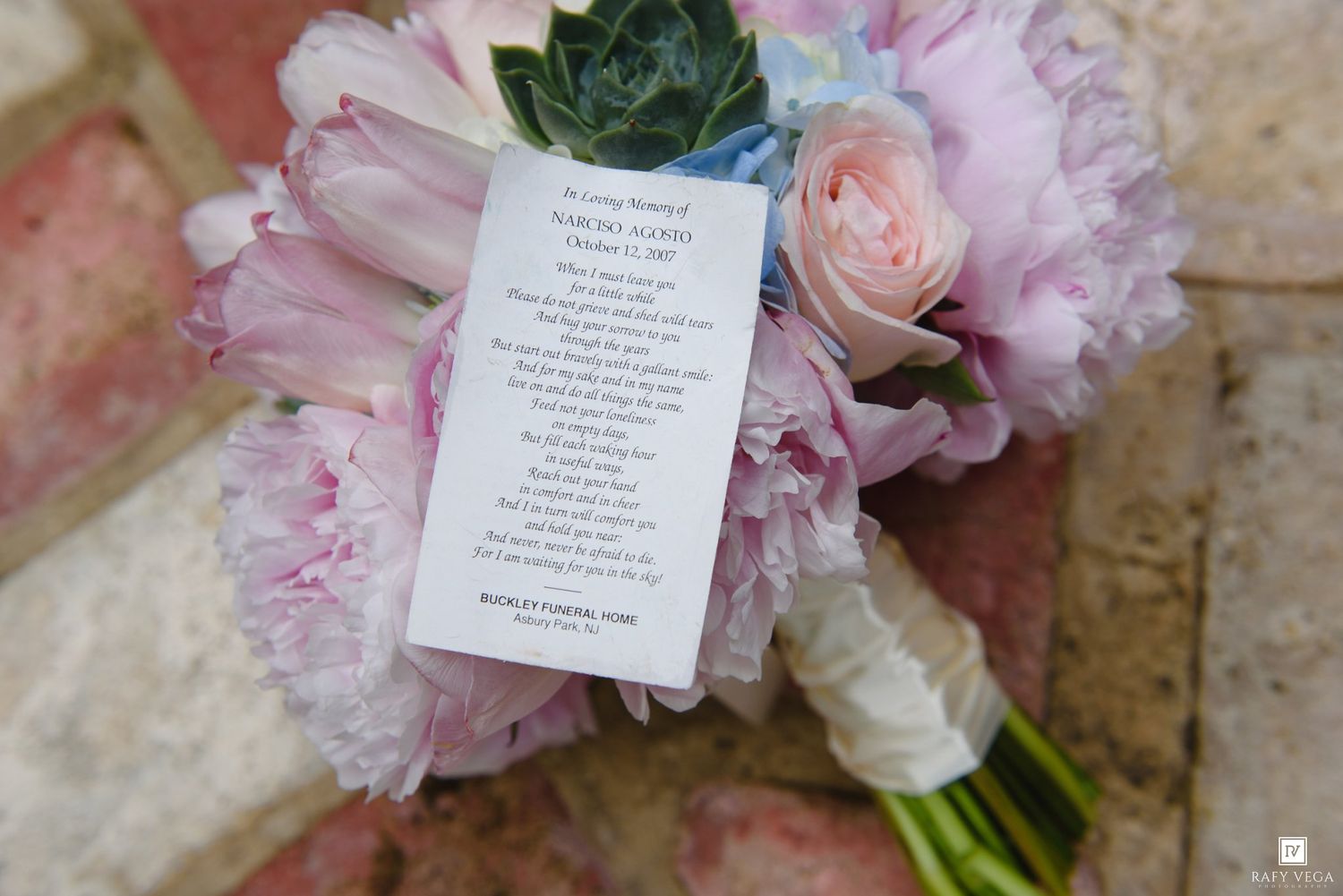 Pink peony and rose wedding bouquet with a poem card on a brick surface.