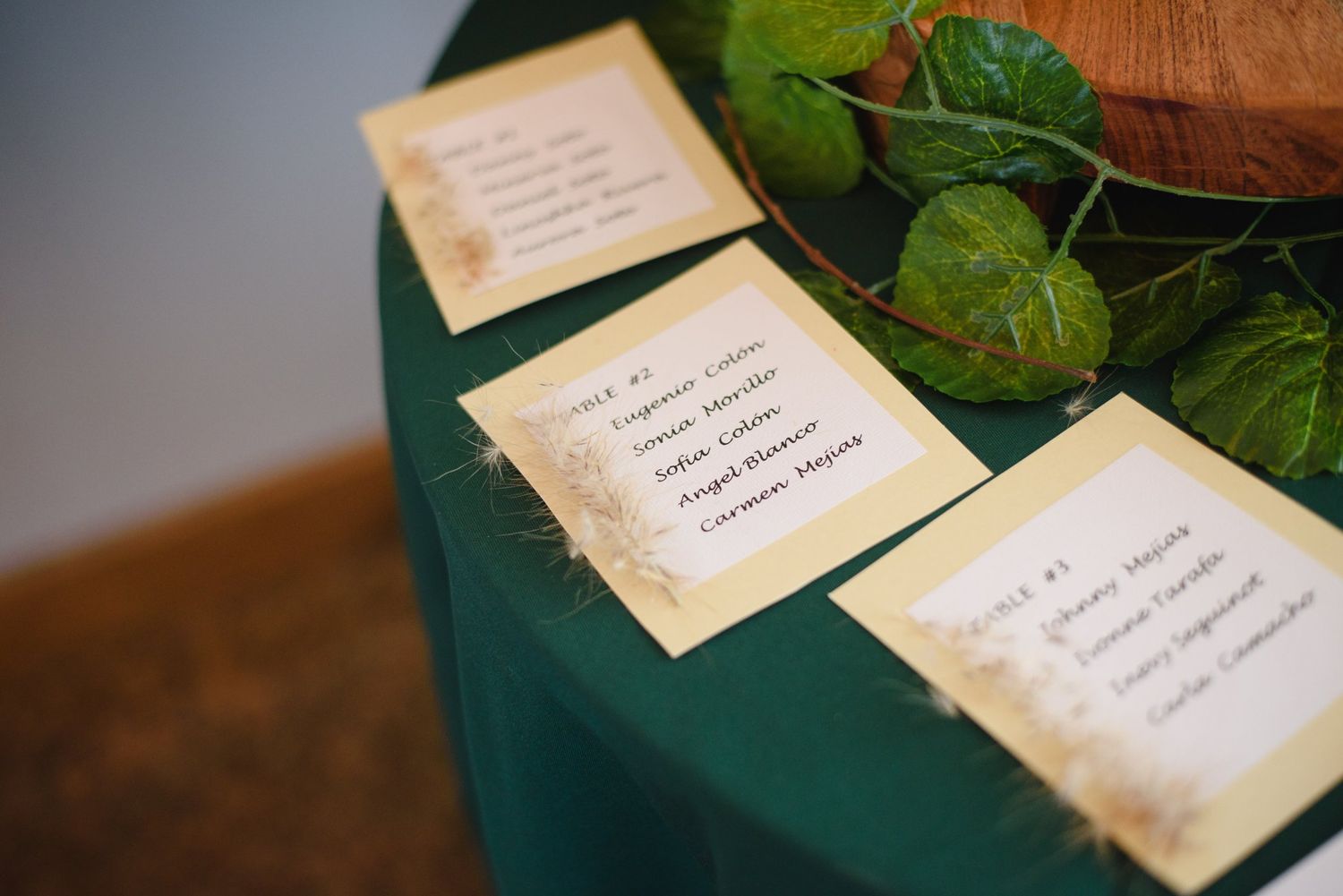 Elegant wedding seating chart cards displayed on a green tablecloth with ivy leaf decorations at a reception venue.