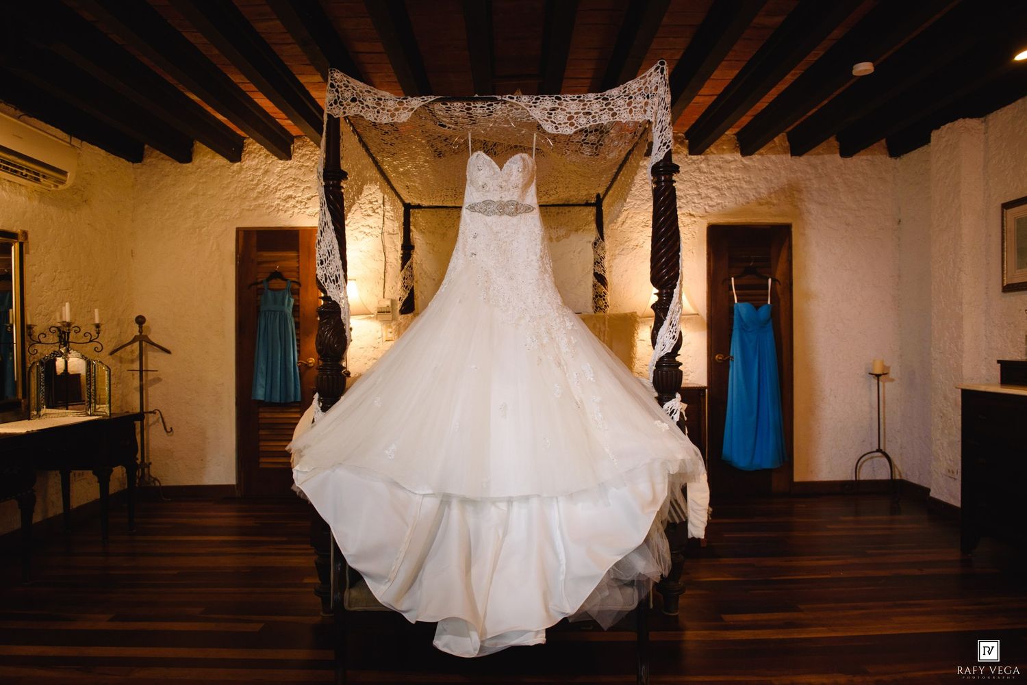 Elegant strapless ball gown wedding dress displayed on a four-poster bed in a rustic wood-beamed room.