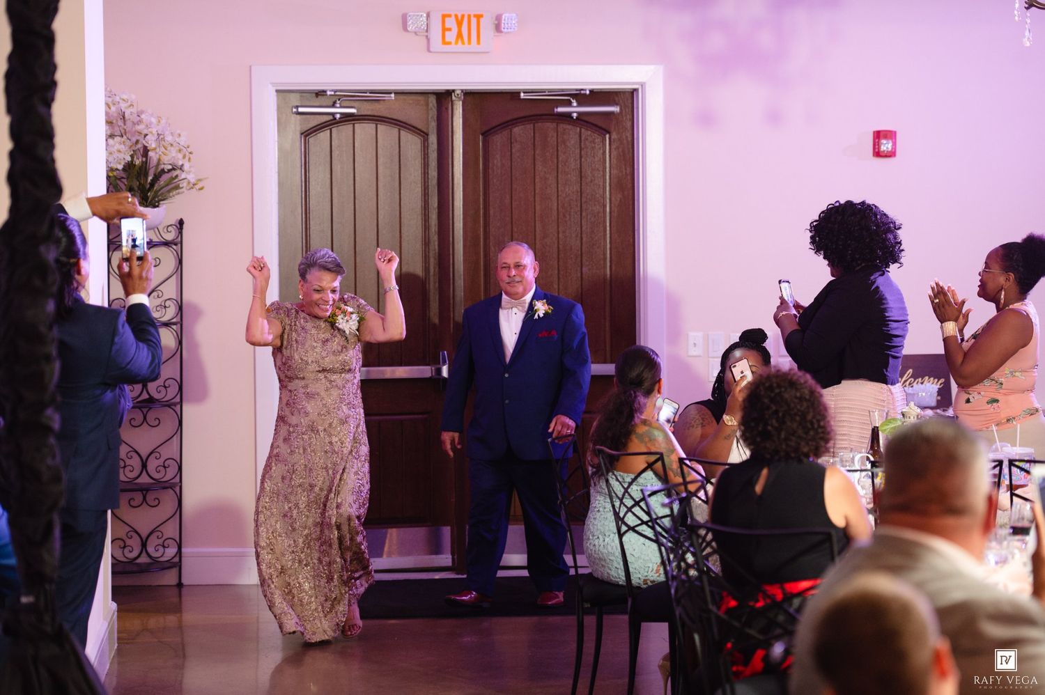 Couple makes grand entrance at wedding reception, guests applaud as they enter elegant ballroom venue.