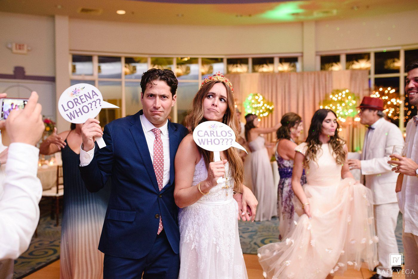 Bride and groom holding fun photo booth signs at their wedding reception on a decorated dance floor.