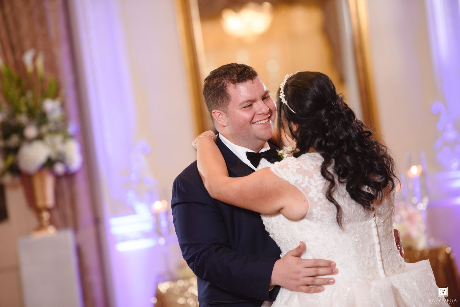 Bride and groom share a joyful first dance at elegant wedding reception with purple uplighting.